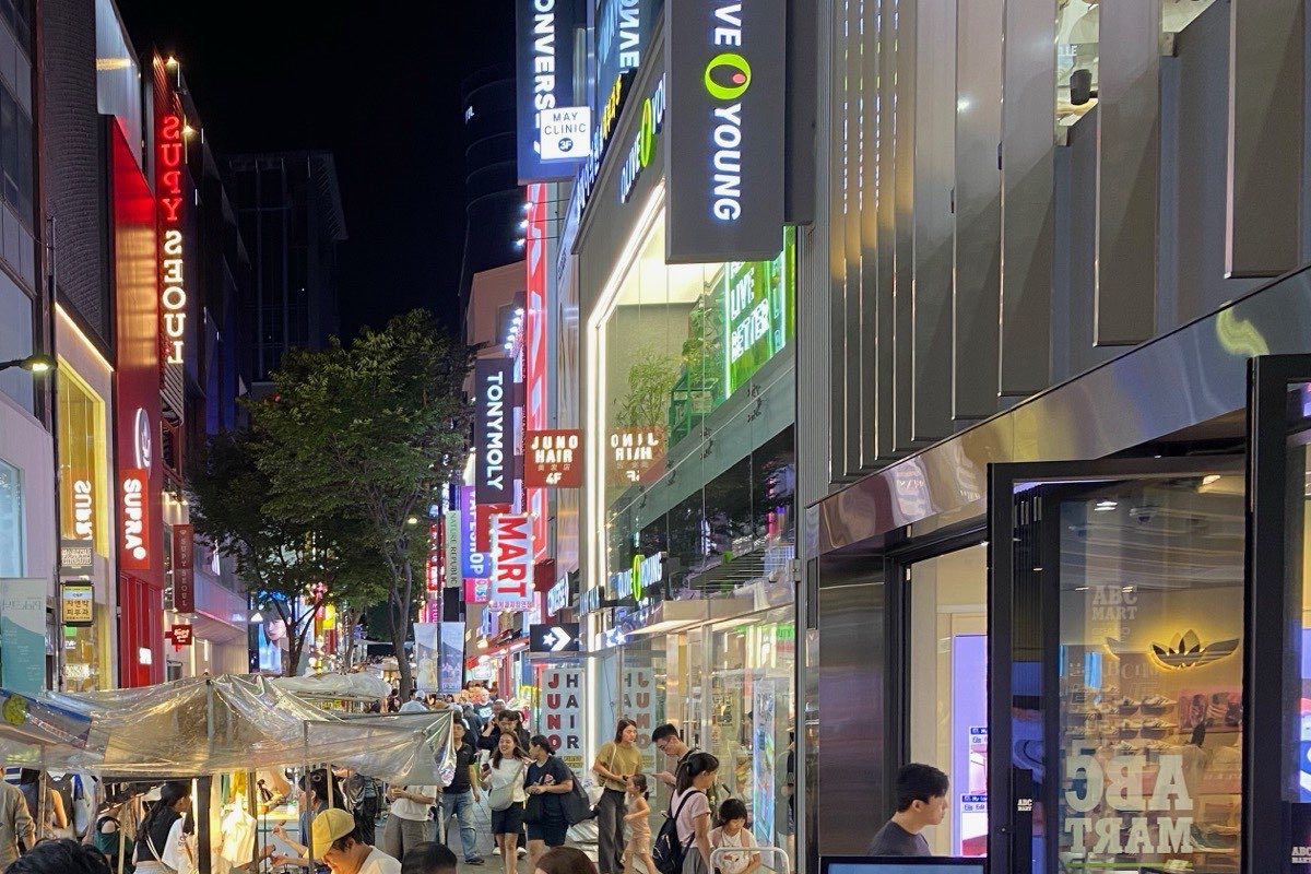 夕方の明洞の買い物通りの人波と屋台。右側に縦型のオリーブヤングの看板